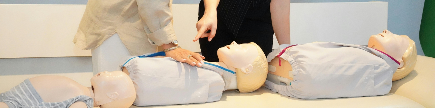 Two women demonstrate CPR techniques on mannequins during a training session indoors.