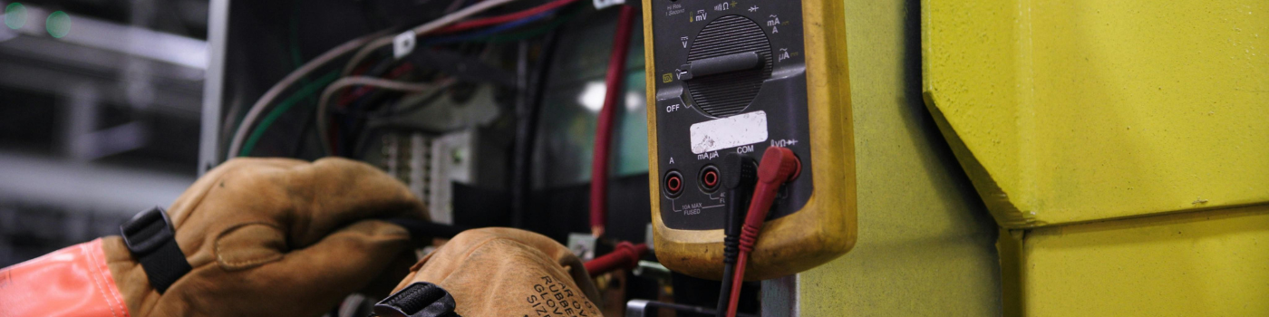 Electrician using a multimeter to fix industrial control panel wiring.