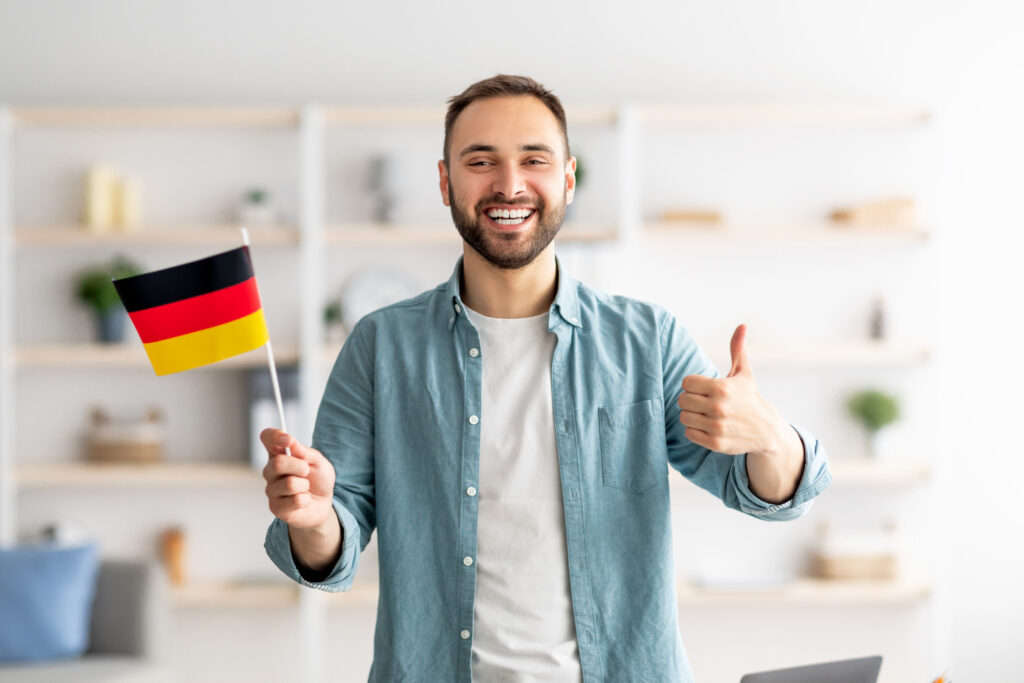 une photo de stock représentant un homme souriant tenant un petit drapeau allemand et faisant un signe de pouce levé