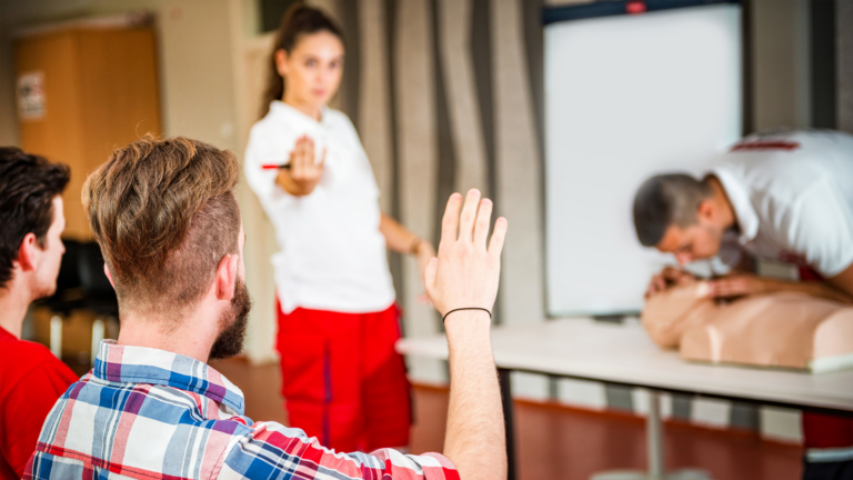 un cours de formation aux premiers secours, où un formateur guide des participants qui s'exercent sur un mannequin de réanimation.