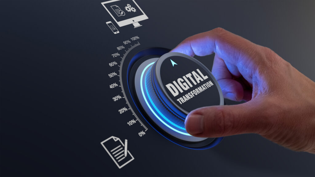 Une main humaine tourne un cadran rotatif futuriste marqué "DIGITAL TRANSFORMATION". Le bouton, éclairé d'un bleu néon, pointe vers une échelle de pourcentage, symbolisant la progression et le contrôle du processus de numérisation d'une entreprise.